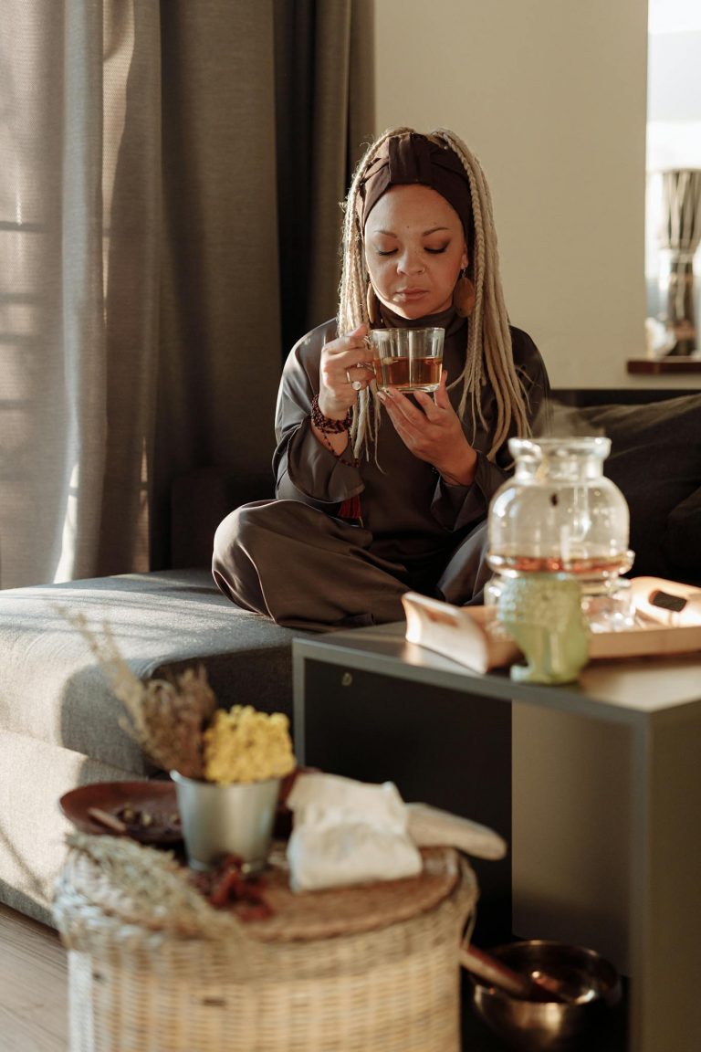 A woman with braided hair relaxes and enjoys a cup of tea in a peaceful living space.