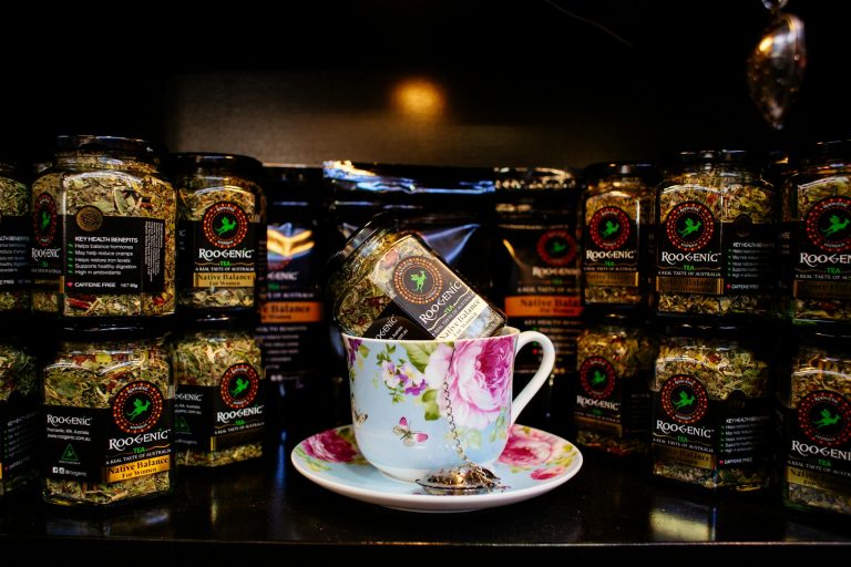 Elegant floral teacup with Roogenic herbal tea jars in a cozy indoor setting.