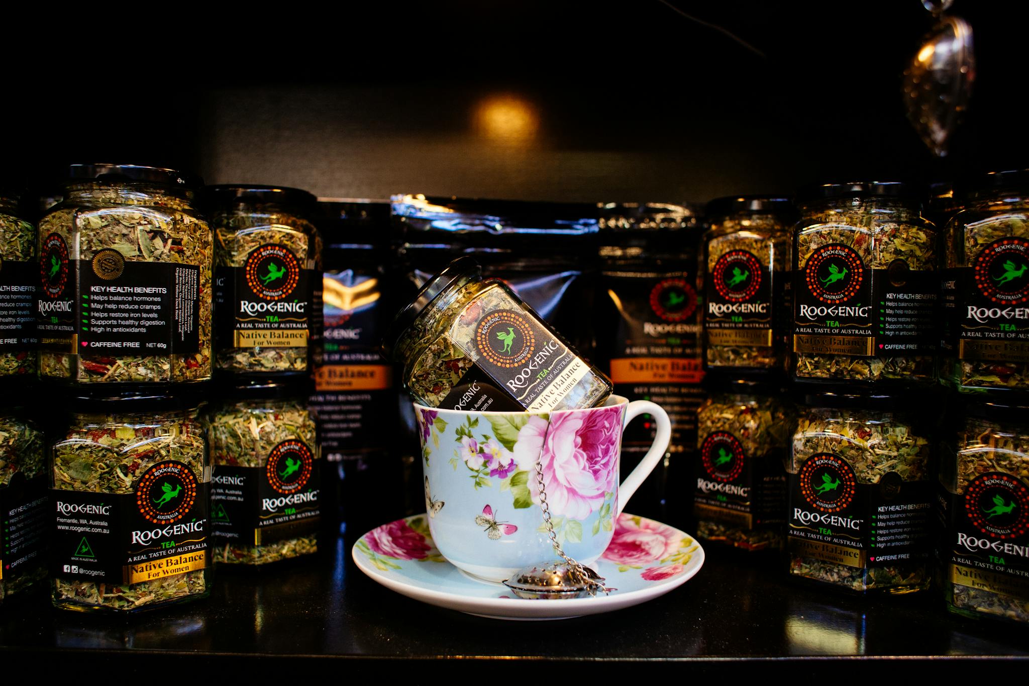 Elegant floral teacup with Roogenic herbal tea jars in a cozy indoor setting.